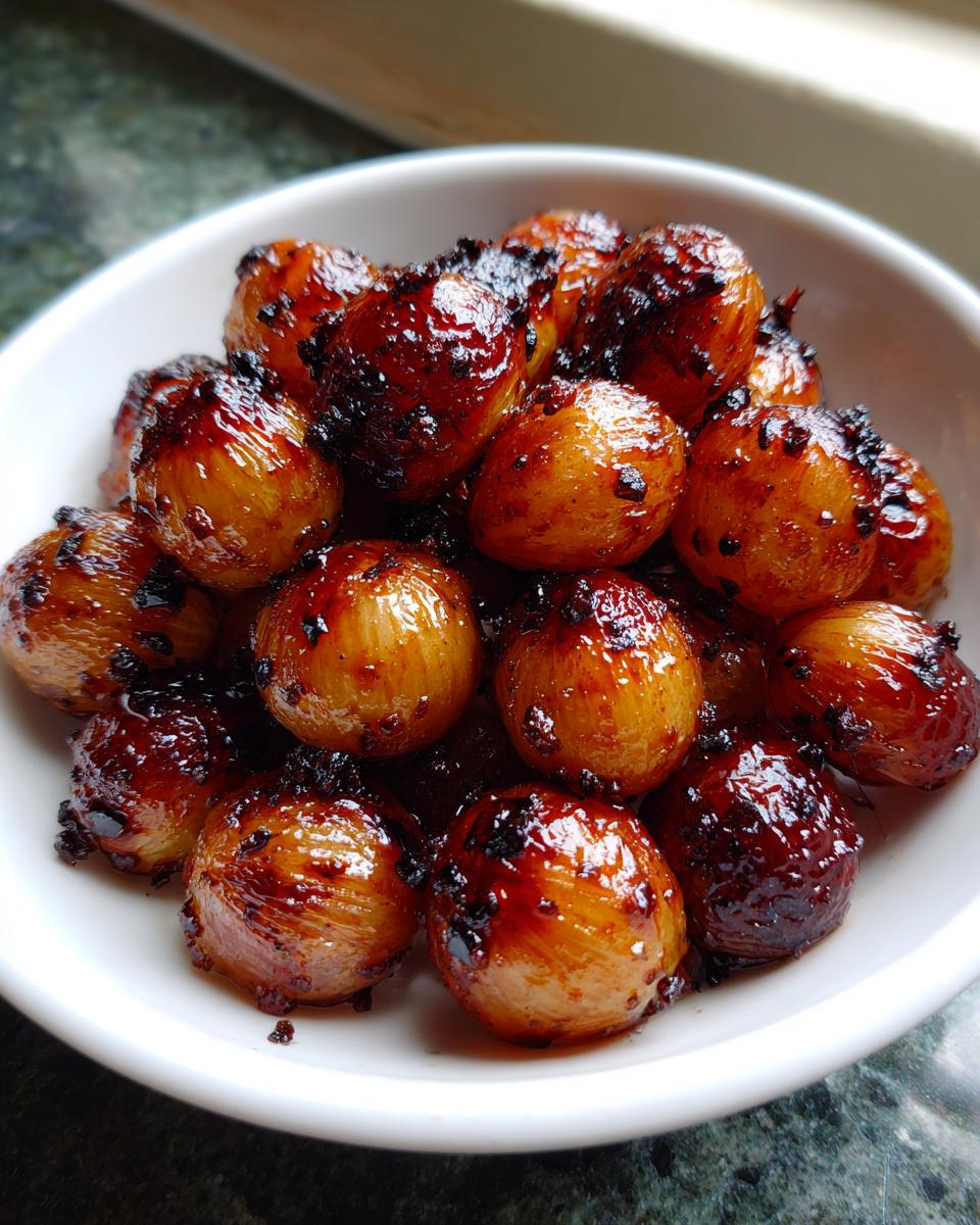 A close-up of glossy, caramelized Air Fryer Pearl Onions piled high in a small white bowl.