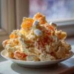 A mound of creamy Ambrosia Fruit Salad topped with mandarin oranges and mini marshmallows.