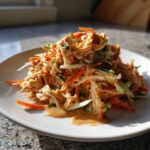 A mound of shredded chicken, carrots, and cucumber tossed in a creamy peanut sauce, served as Asian Peanut Chicken Salad.