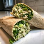 Two halves of a whole wheat wrap filled with creamy chicken salad, romaine lettuce, and chunks of avocado, showcasing the Avocado Chicken Caesar Salad Wraps filling.