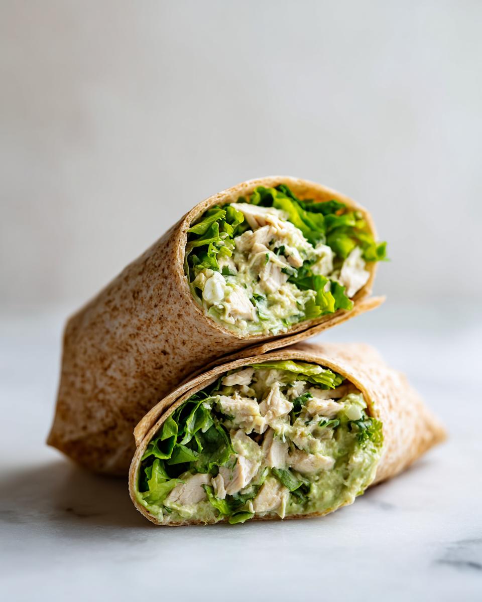 Two halves of an Avocado Chicken Caesar Salad Wrap stacked, showing creamy filling and crisp lettuce.