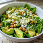 A vibrant close-up of an Avocado Feta Chickpea Bowl featuring green lettuce, sliced avocado, roasted chickpeas, and crumbled white feta cheese.