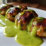 Close-up of golden brown Baked Salmon Meatballs drizzled generously with bright green Creamy Avocado Sauce.