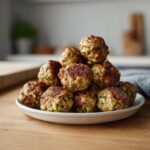 A stack of golden-brown Baked Turkey Zucchini Meatballs piled high on a small white plate.