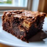 A rich, fudgy square of Banana Bread Brownies with a crackly top, served on a white plate.