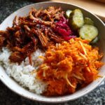 A close-up of a single serving of BBQ Chicken Bowls with sweet potatoes, white rice, pickled onions, and dill pickles.