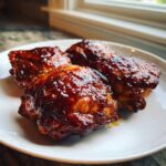 Four succulent BBQ Ranch Chicken Thighs coated in a thick, shiny glaze, served on a white plate.