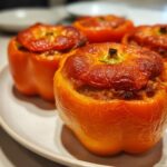 Close-up of baked orange Beef And Rice Stuffed Bell Peppers with browned tops on a white plate.