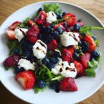 Close-up of a fresh Berries Burrata Salad featuring strawberries, blueberries, blackberries, and dollops of burrata cheese.