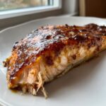 A close-up of a perfectly cooked Bourbon Peach Roasted Salmon fillet with a thick, shiny glaze on a white plate.