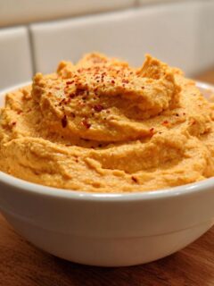 A close-up of creamy Butternut Squash Dip With Air Fryer Roasted Garlic topped with red pepper flakes in a white bowl.