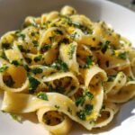 Close-up of glossy Calamarata Heirloom Pasta tossed with fresh parsley and bright yellow lemon zest.