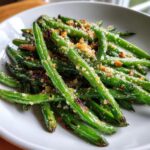 Bright green, glossy green beans tossed with golden breadcrumbs and garlic, served in a white bowl.
