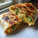 Close-up of a Cheesy Jalapeno Onion Tortilla cut in half, showing melted cheese, onions, and green peppers.