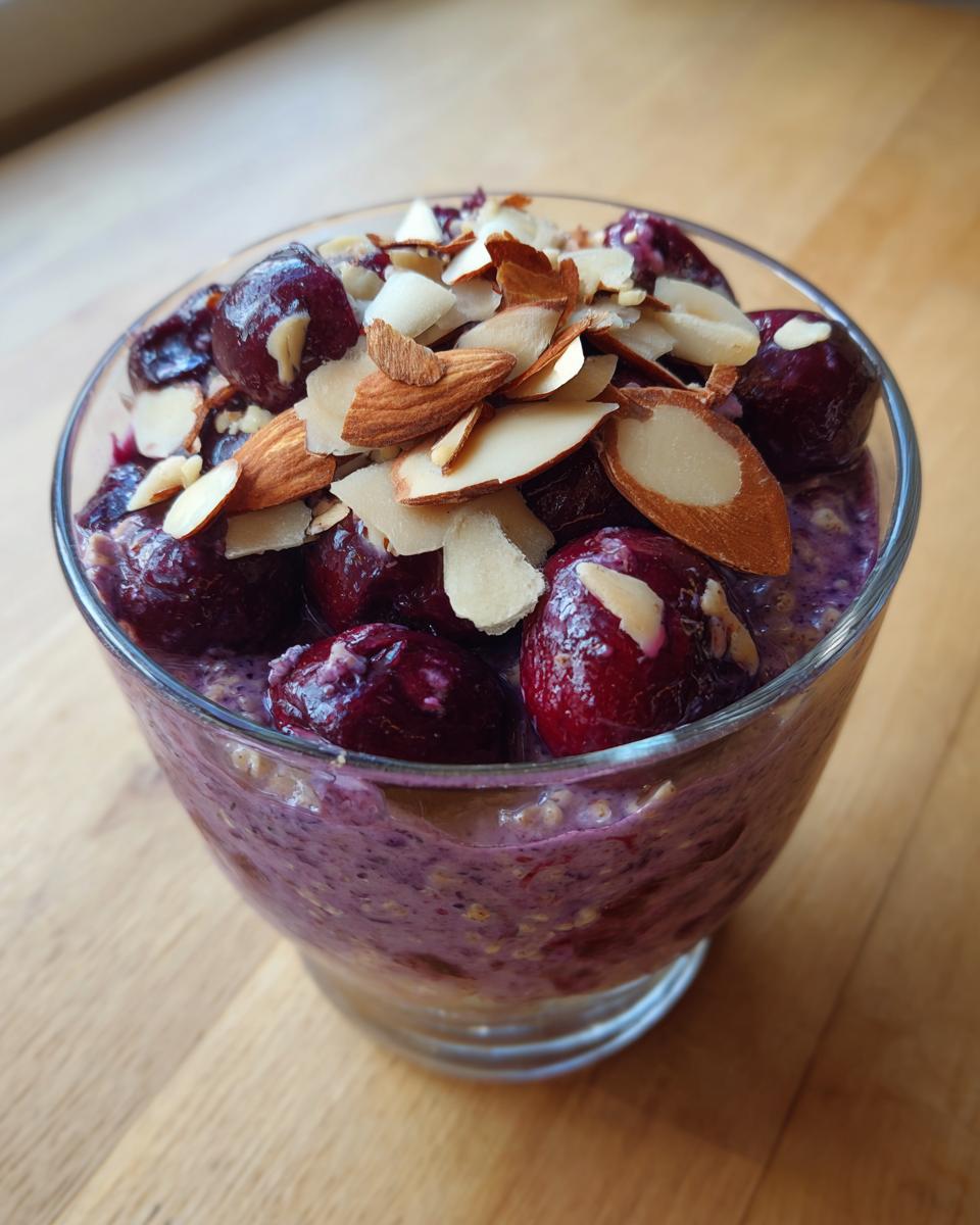 A glass serving of Cherry Almond Overnight Oats topped with whole cherries and sliced almonds.