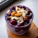 Close-up of Cherry Almond Overnight Oats topped with whole and sliced almonds over dark cherries.