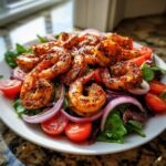 A vibrant plate of Chili Lime Shrimp Salad featuring seasoned shrimp over mixed greens with sliced red onions and cherry tomatoes.
