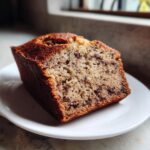A close-up slice of moist Chocolate Banana Bread studded with chocolate chips, served on a white plate.