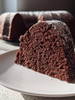 Close-up of a moist slice of Chocolate Bundt Cake dusted with powdered sugar, with the rest of the cake blurred in the background.