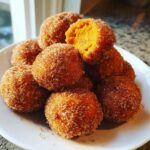 A pile of golden Churro Pumpkin Bites coated in cinnamon sugar, one broken open showing the soft pumpkin interior.