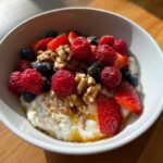 A white bowl filled with Cottage Cheese Breakfast Bowls topped with fresh raspberries, blueberries, strawberries, walnuts, and cinnamon.