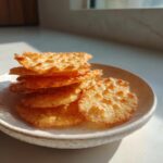 A stack of crispy, golden-brown Cottage Cheese Chips resting on a small ceramic plate in bright sunlight.