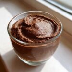 A close-up of rich, dark brown Cottage Cheese Chocolate Mousse swirled inside a clear glass cup.
