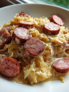 A white bowl filled with creamy kielbasa and sauerkraut, topped with sliced smoked sausage.