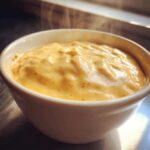 Close-up of hot, steaming Creamy White Cheddar Beer Cheese Dip in a white bowl, showing its rich texture.