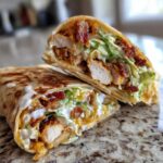 A close-up of a Crispy Chicken Bacon Ranch Wrap cut in half, showing crispy chicken, bacon, lettuce, and ranch dressing.