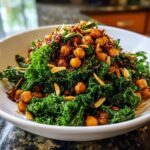 A vibrant serving of Crispy Chickpea Kale Salad piled high in a white bowl, topped with roasted chickpeas and slivered almonds.