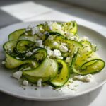 Close-up of a fresh Cucumber Ribbon Feta Salad featuring thinly shaved ribbons topped with crumbled feta and herbs.
