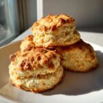 A stack of four golden-brown Easy Baking Powder Drop Biscuits with flaky layers, sitting on a white plate.