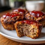 Close-up of Easy Mini Meatloaf Muffins with a bite taken out, showing the texture and ketchup glaze.