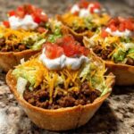 Close-up of several Easy Taco Salad Cups filled with seasoned beef, lettuce, cheese, sour cream, and diced tomatoes.