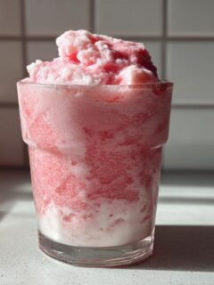 A tall glass filled with a thick, icy Everyday Strawberry Coconut Smoothie, showing layers of pink ice and white coconut milk.