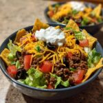 A close-up of an Everyday Taco Salad Bowl featuring seasoned ground beef, lettuce, tomatoes, shredded cheese, black olives, and sour cream.