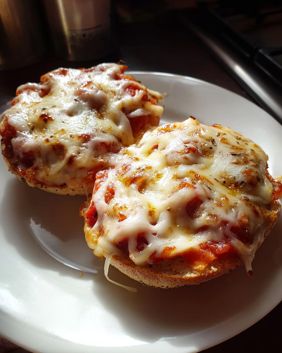 Two freshly baked Freezer Bagel Pizzas For Busy Nights topped with bubbling, melted mozzarella cheese on a white plate.