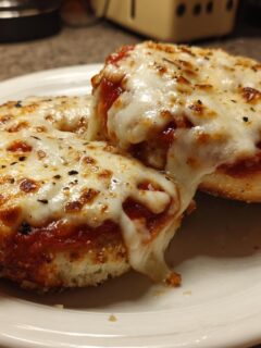 Two freshly baked Freezer Bagel Pizzas For Busy Nights topped with bubbling, melted mozzarella cheese on a white plate.