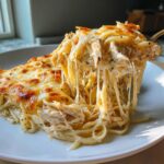 A serving of Freezer Friendly Chicken Alfredo Bake showing extreme cheese pull with shredded chicken and pasta.