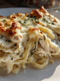 A close-up serving of Freezer Friendly Chicken Alfredo Bake with melted, browned cheese and herbs.