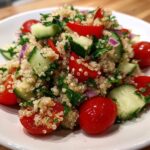 A vibrant close-up of Fresh Quinoa Lunch Salad featuring cooked quinoa, halved cherry tomatoes, chopped cucumber, and red onion.