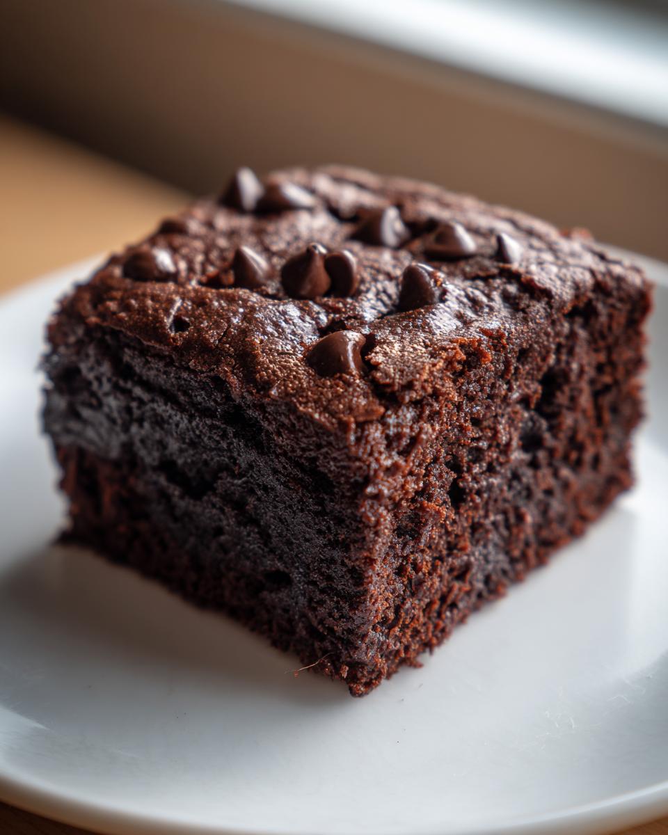 A single, rich, dark square of Fudgy Sweet Potato Brownies topped with chocolate chips on a white plate.