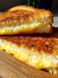 Two halves of a perfectly golden brown Garlic Bread Grilled Cheese sandwich showing melted cheese.