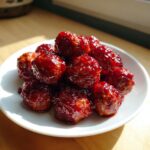 A pile of glistening Cranberry Meatballs coated in a thick, dark red sauce, served on a small white plate.