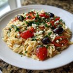 Close-up of a serving of Greek Orzo Salad featuring pasta, cherry tomatoes, feta, and olives.
