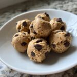 Close-up of several balls of edible Greek Yogurt Cookie Dough studded with mini chocolate chips on a white plate.
