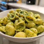 A white bowl filled with shell pasta coated in vibrant Green Goddess Mac And Cheese sauce, topped with grated cheese.