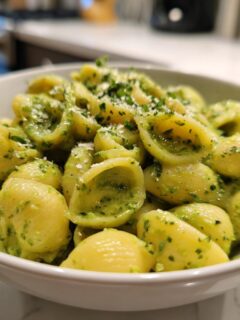 A white bowl filled with shell pasta coated in vibrant Green Goddess Mac And Cheese sauce, topped with grated cheese.