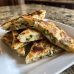 A stack of freshly grilled Garlic Scallion Pancakes cut into wedges on a white plate.